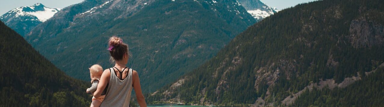 A mother with two children enjoys a scenic mountain and lake view during a sunny outdoor hike.